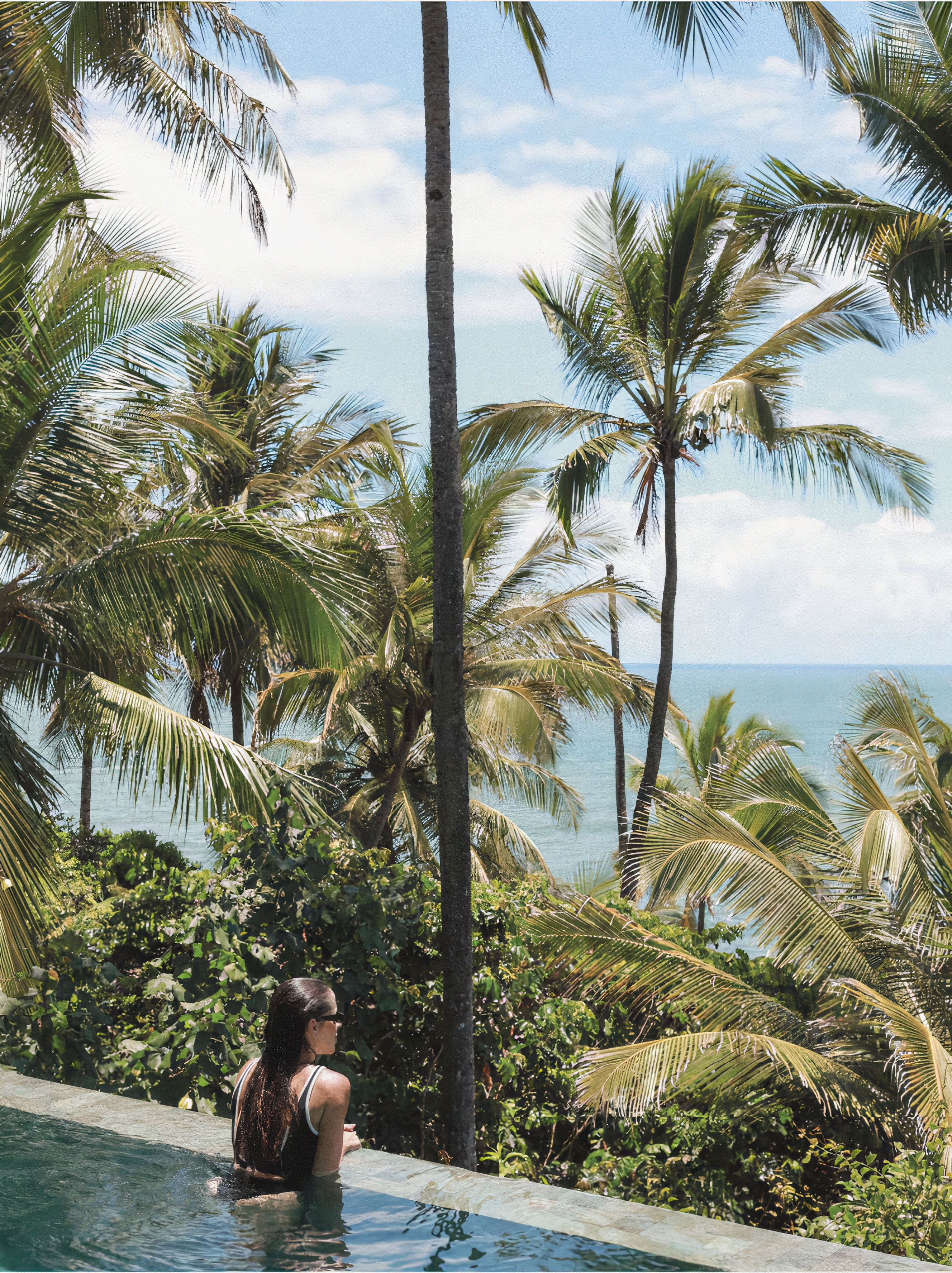 Woman in infinity pool with ocean and jungle view